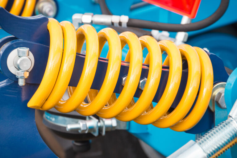 Big and hard steel yellow spring as part and detail of blue industrial or agricultural machine